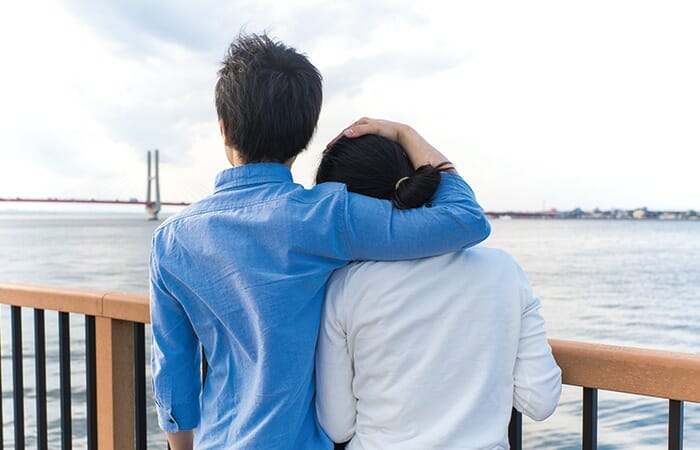 港で寄り添い肩を組みながら海を眺めるカップル