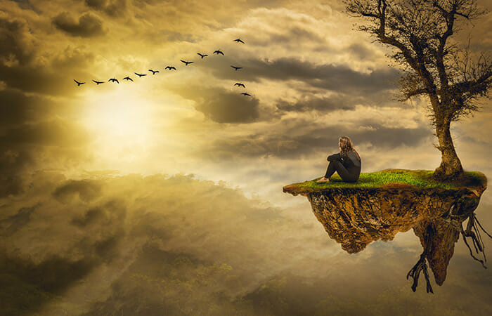 空に浮かぶスピリチュアルな岩に膝を抱えて独り寂しく空を眺める男性
