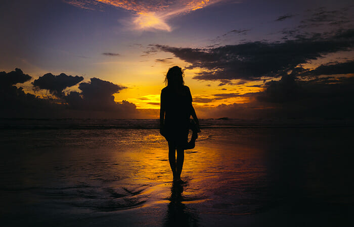 一人寂しく夕焼けの海岸を海に向かって歩く女性
